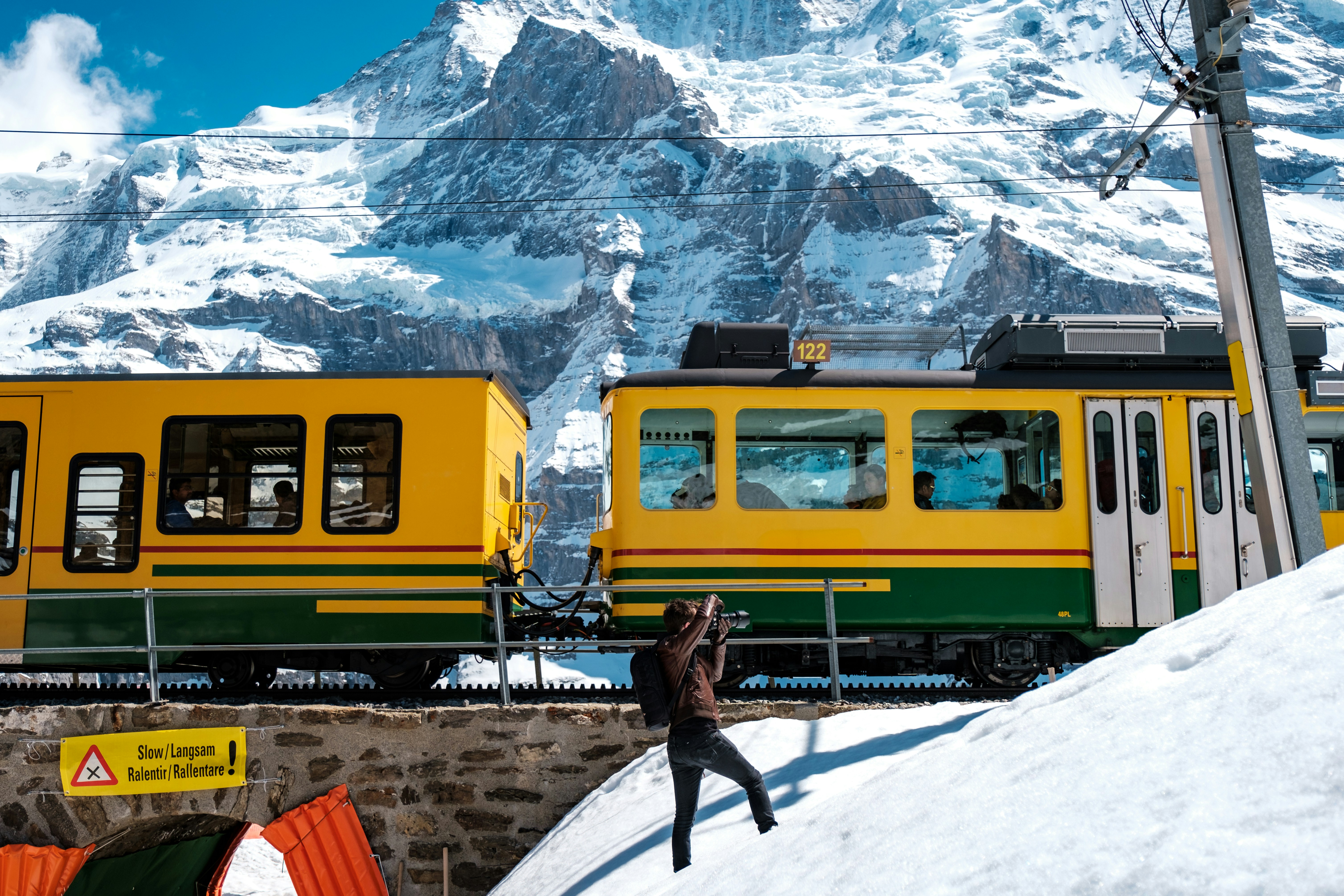 person in black jacket standing near yellow train during daytime, Photographing the train as it heads up to Jungfraujoch, the highest train station in Europe.