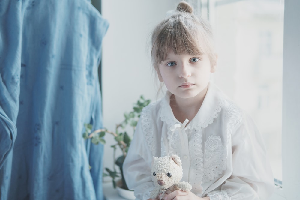 fille en robe blanche tenant un ours blanc jouet en peluche