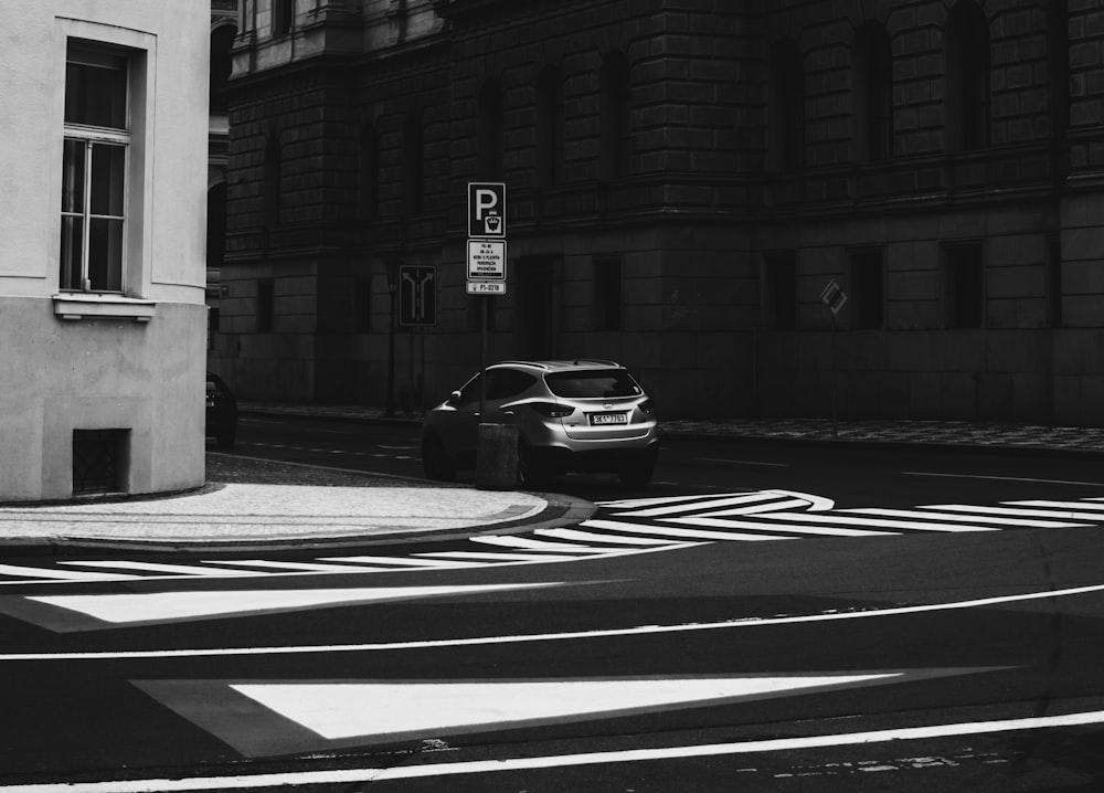 grayscale photo of car parked beside building