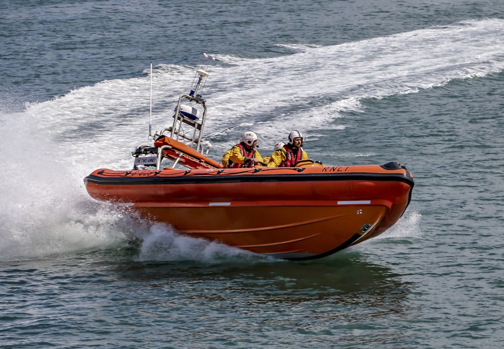 people riding orange and white boat on sea during daytime