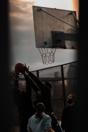 A dynamic basketball game in action with players reaching for the ball under bright gym lights.