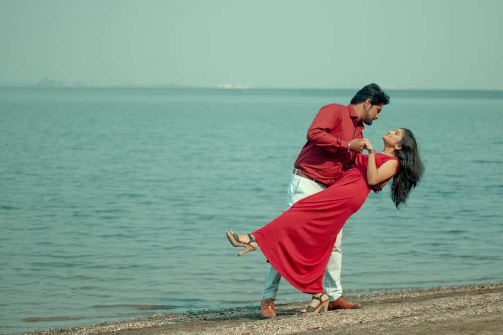 woman in pink dress kissing man in blue dress shirt on beach during daytime