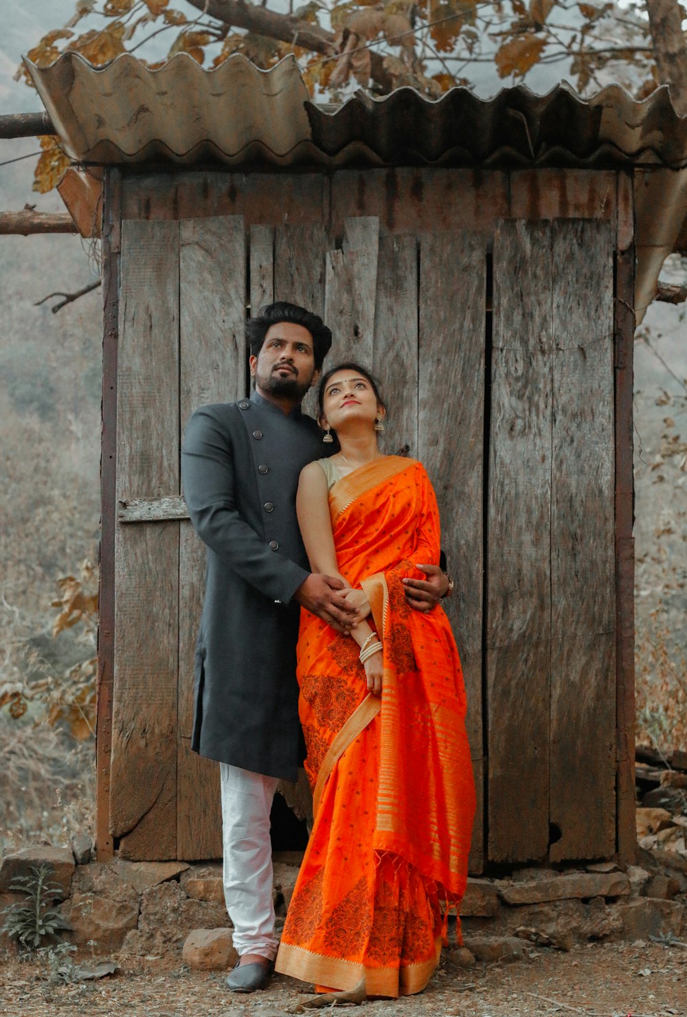 man in grey dress shirt and orange scarf standing beside woman in orange and yellow dress