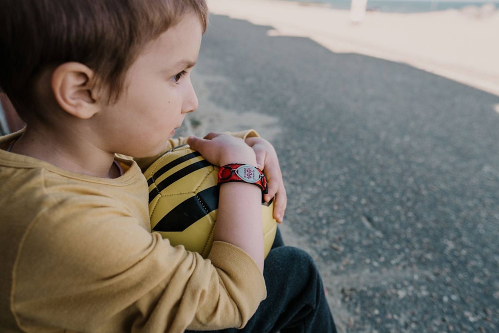 boy in yellow and black striped t-shirt and blue denim jeans sitting on gray concrete