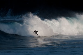 A surfer skillfully rides a large, crashing wave with water splashing around, conveying a sense of motion and adventure.