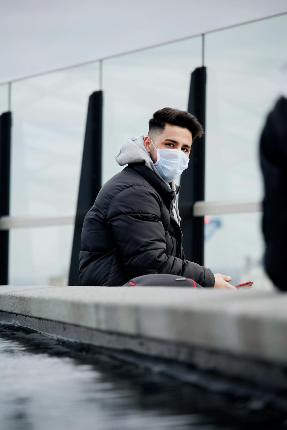 man in black jacket and white face mask sitting on concrete bench