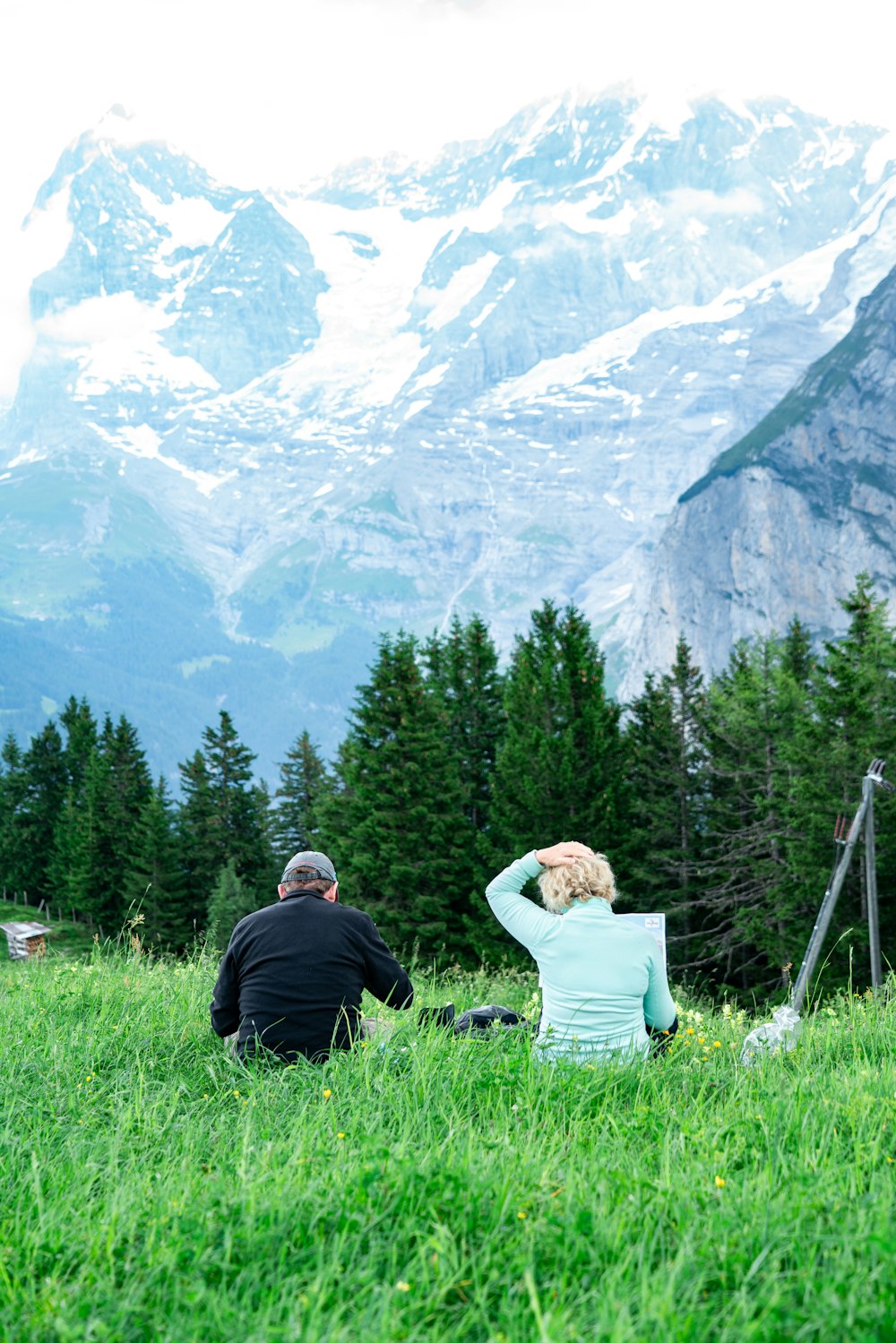 man and woman sitting on grass field near green trees and mountain during daytime