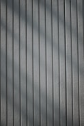 A textured wall with vertical lines, creating a shadow effect. The lines are evenly spaced and run parallel across the entire surface.
