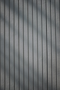 A textured wall with vertical lines, creating a shadow effect. The lines are evenly spaced and run parallel across the entire surface.