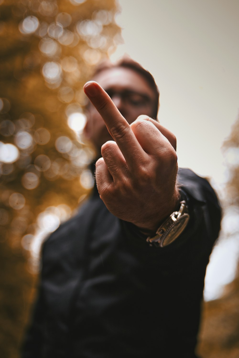 homem em jaqueta preta vestindo relógio de prata mostrando seu dedo médio
