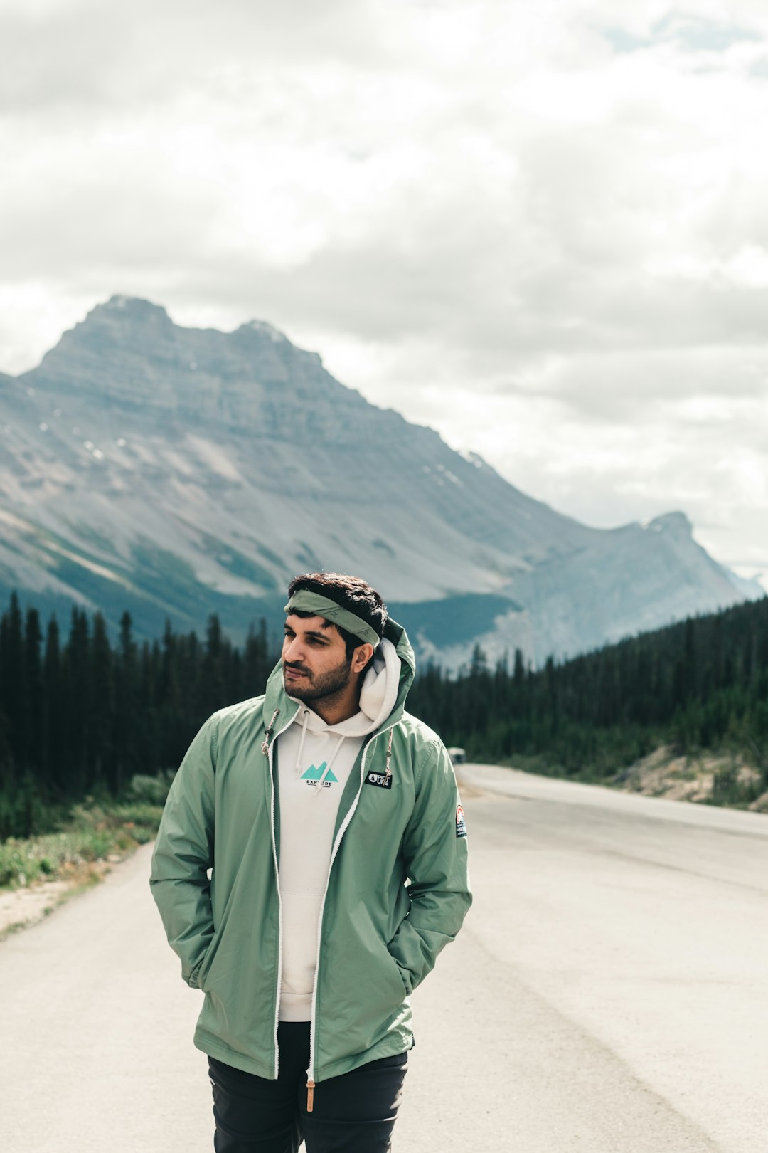 man in green jacket standing on road near green trees and mountain during daytime