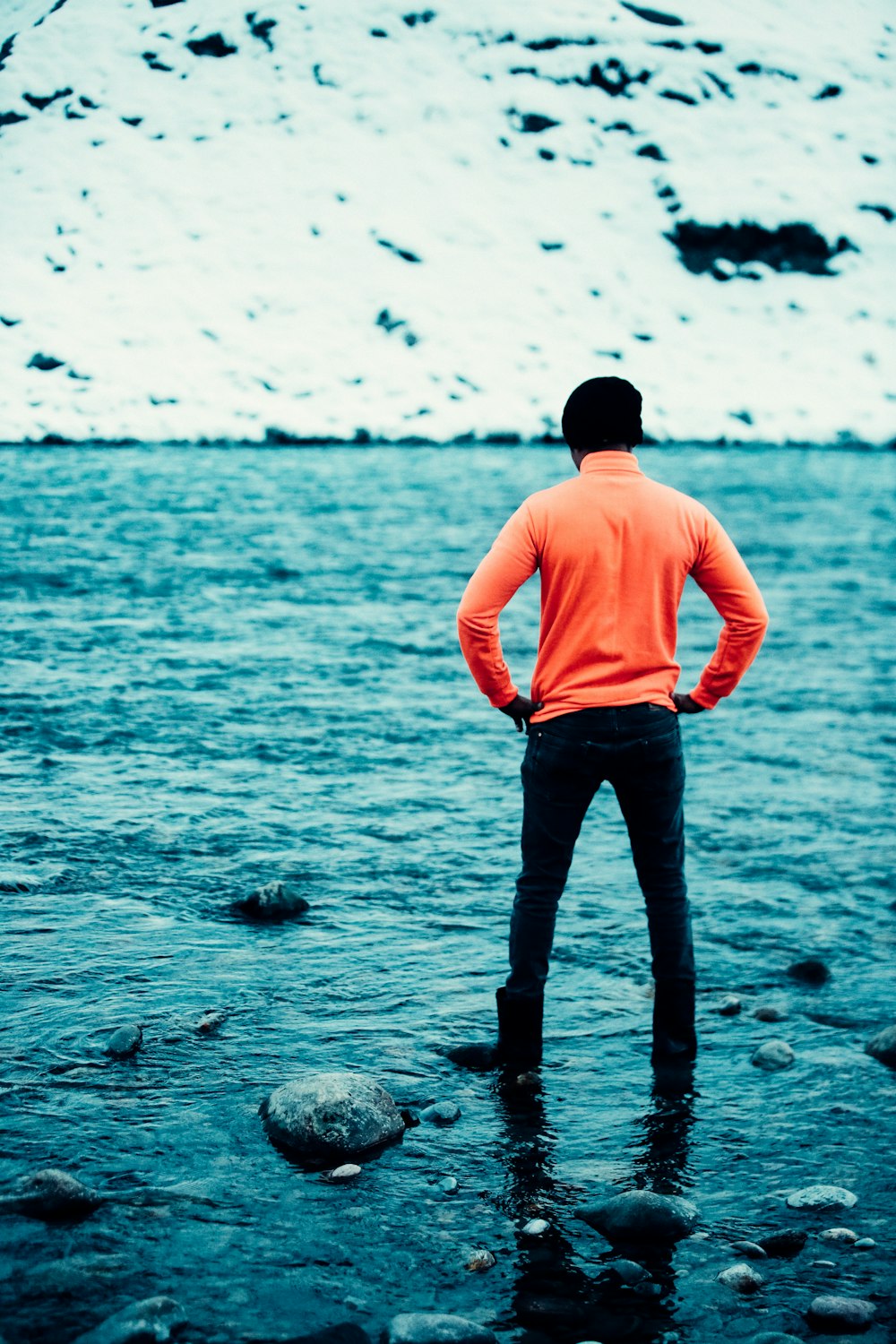 homme en chemise rose et pantalon noir debout sur le rivage rocheux pendant la journée