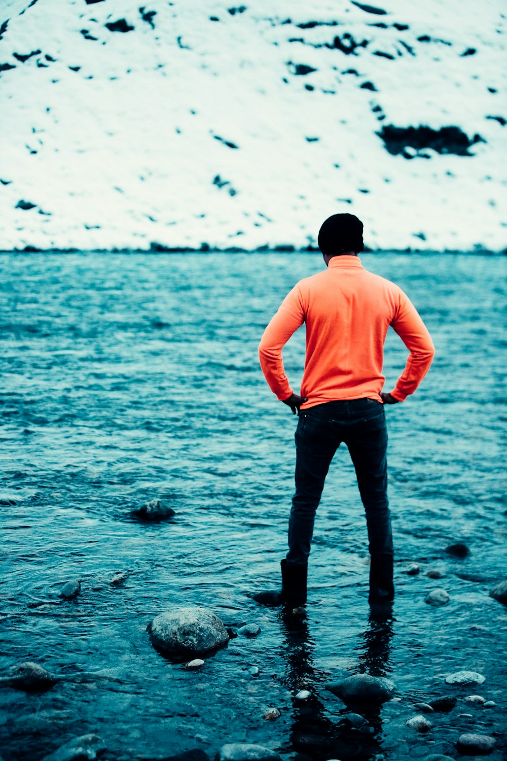 man in pink shirt and black pants standing on rocky shore during daytime