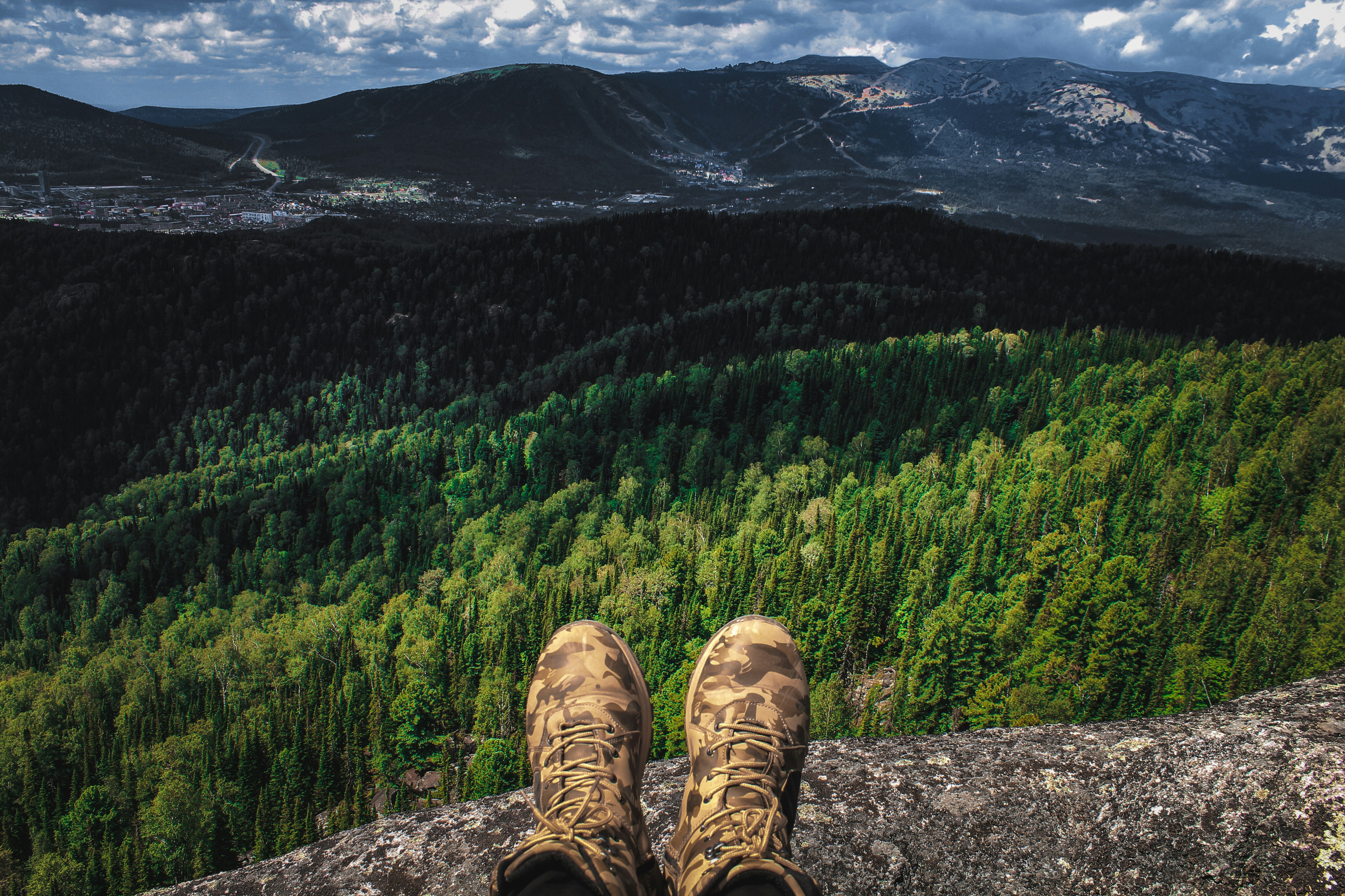 person in brown hiking shoes sitting on rock near green trees during daytime