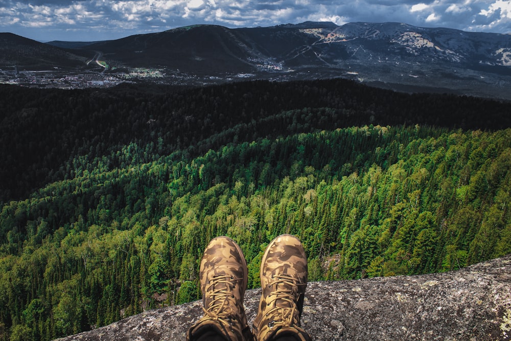 日中、緑の木々の近くの岩の上に座っている茶色のハイキングシューズを履いた人