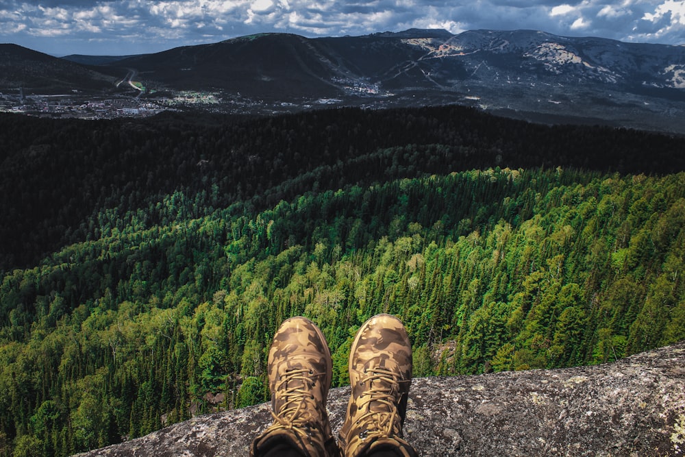 person in brown hiking shoes sitting on rock near green trees during daytime