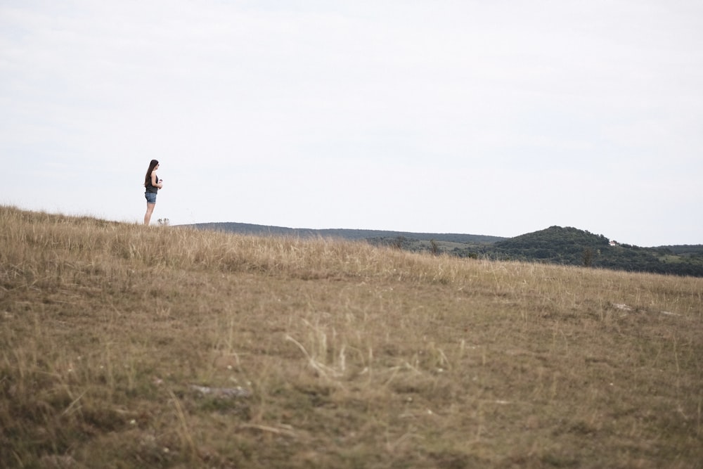 uma mulher em pé no topo de uma encosta coberta de grama