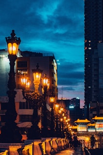 The man walking along a quiet city street at dusk, the glow of street lamps behind him.
