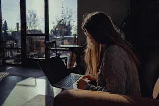 A hopeful job seeker smiling while using a laptop in a cozy, sunlit room.