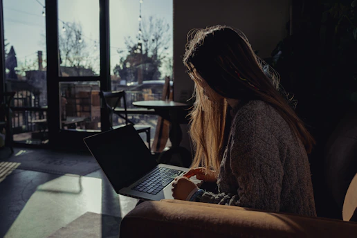 A hopeful job seeker smiling while using a laptop in a cozy, sunlit room.