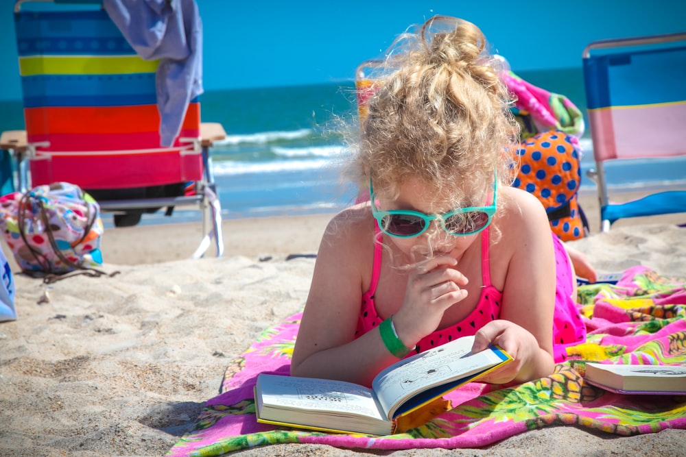 분홍색 탱크탑을 입은 소녀는 낮 동안 해변에서 책을 읽고 있는 안경을 쓰고