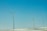 Three wind turbines stand on a snowy landscape under a clear blue sky. The turbines are evenly spaced, with long blades that are designed to capture wind energy.