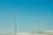 Three wind turbines stand on a snowy landscape under a clear blue sky. The turbines are evenly spaced, with long blades that are designed to capture wind energy.