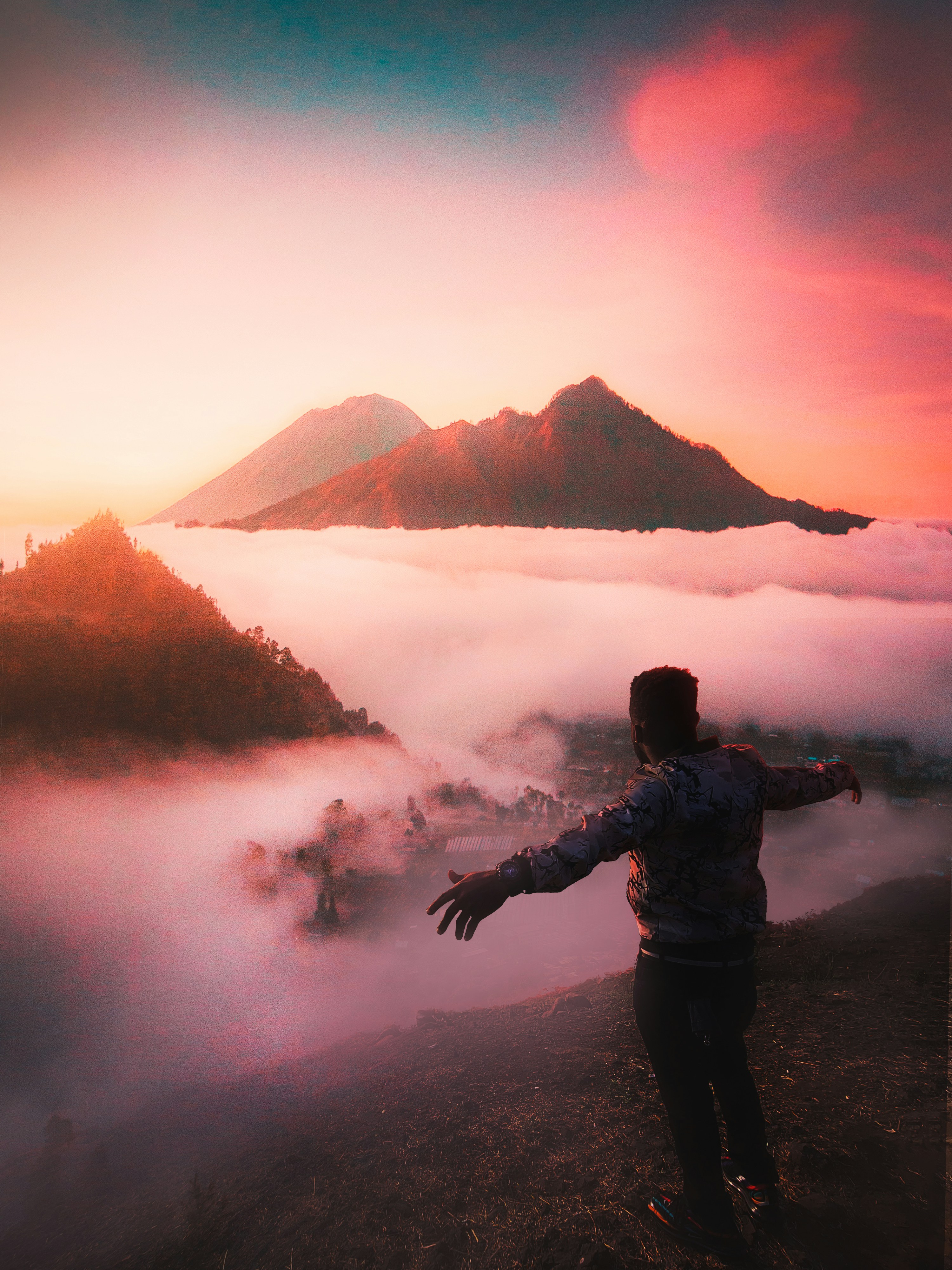 Person standing on mountain summit at dawn, arms outstretched, warm amber sunrise behind them, deep teal sky above, triumphant silhouette against light