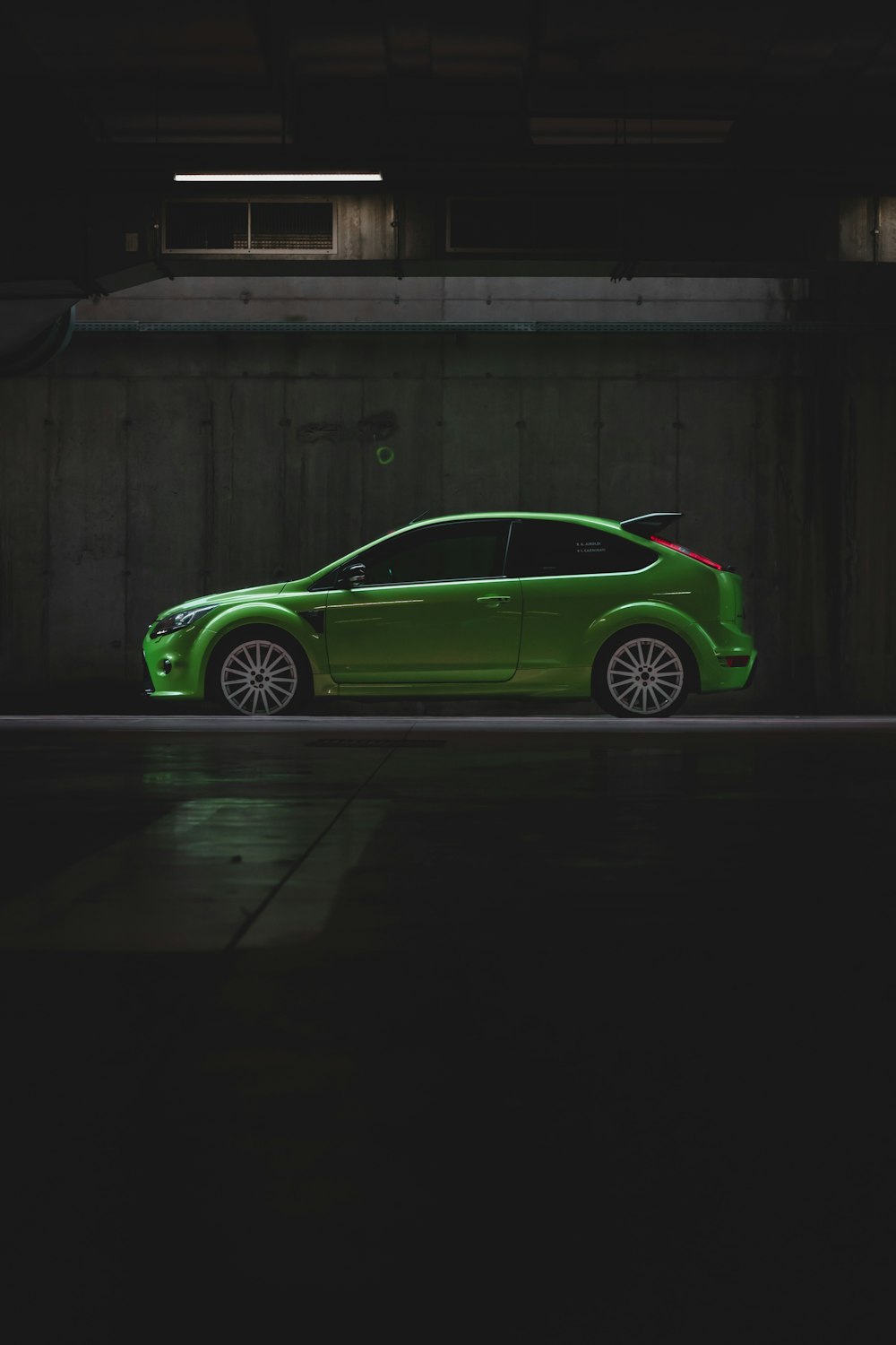 green coupe parked beside brown wooden wall