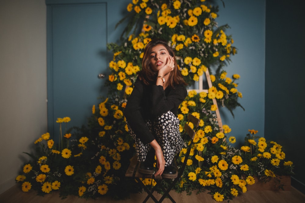 woman in black long sleeve shirt sitting on black metal chair surrounded by yellow flowers