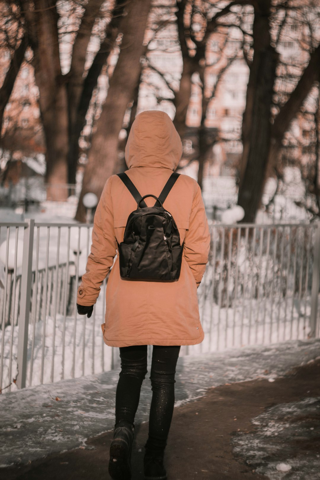 person in orange hoodie and black pants standing on snow covered ground during daytime