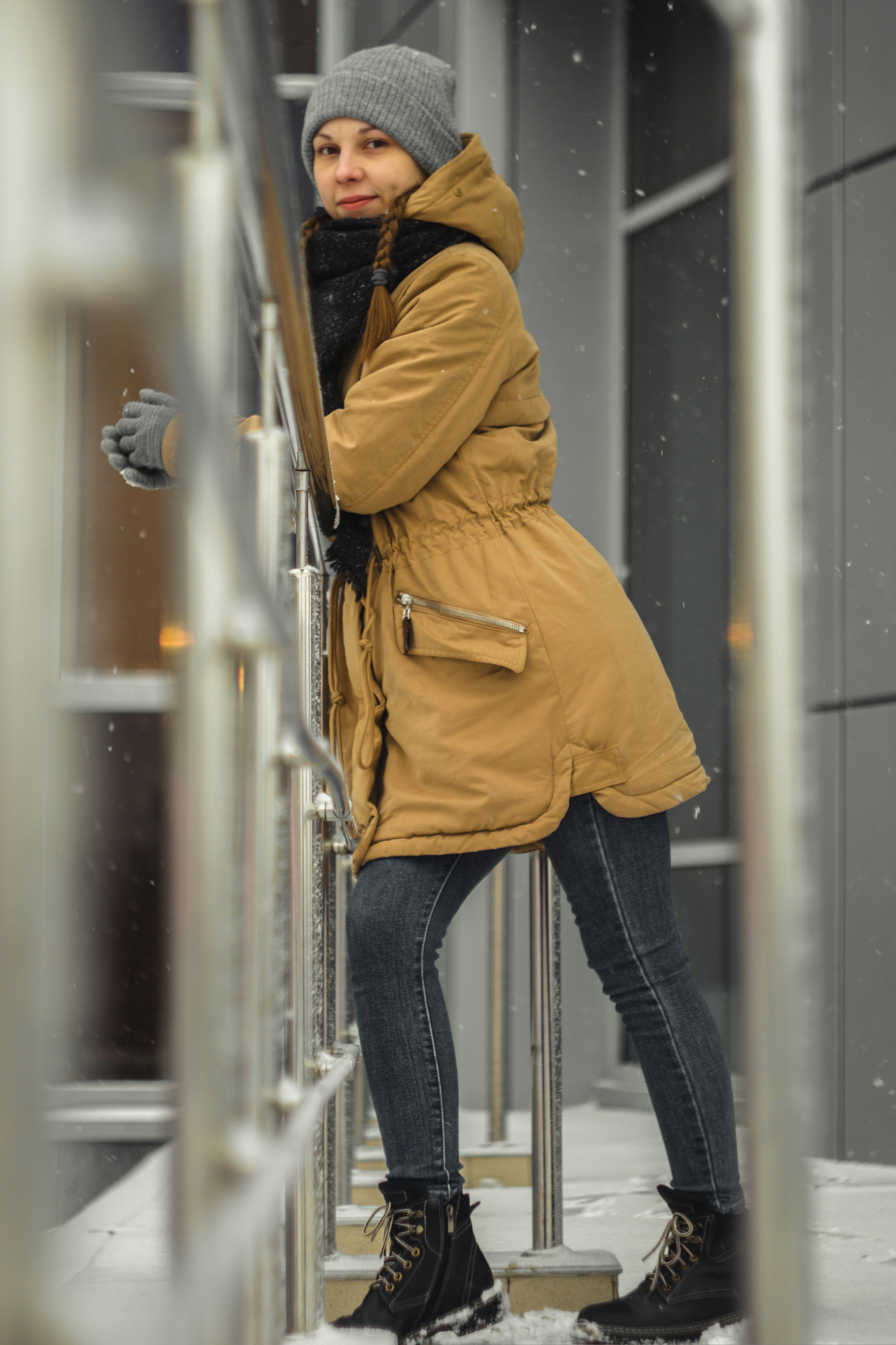 person in brown jacket and blue denim jeans standing in front of glass window