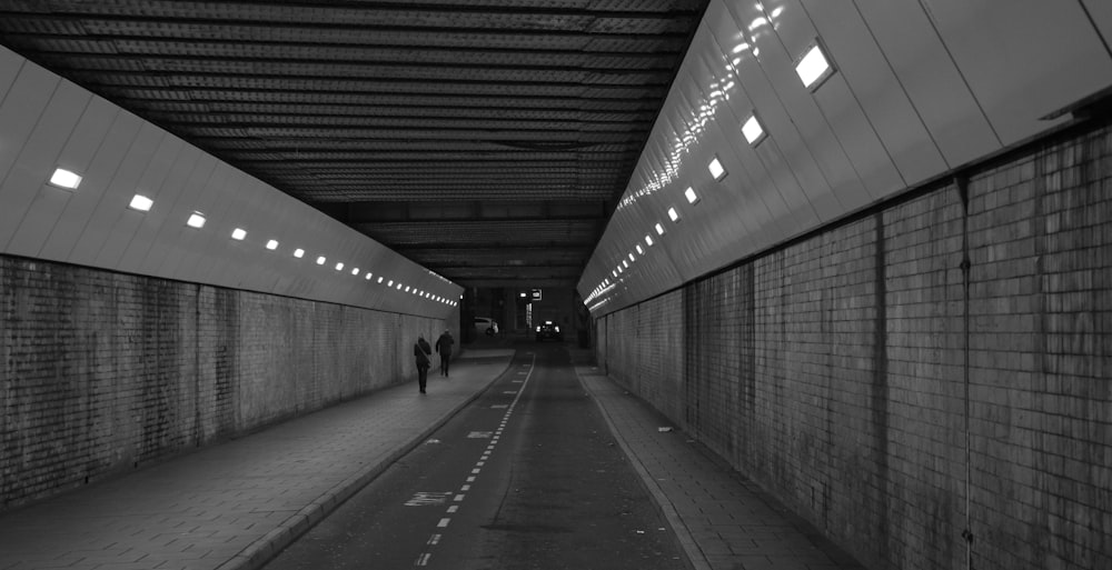 grayscale photo of man walking on tunnel