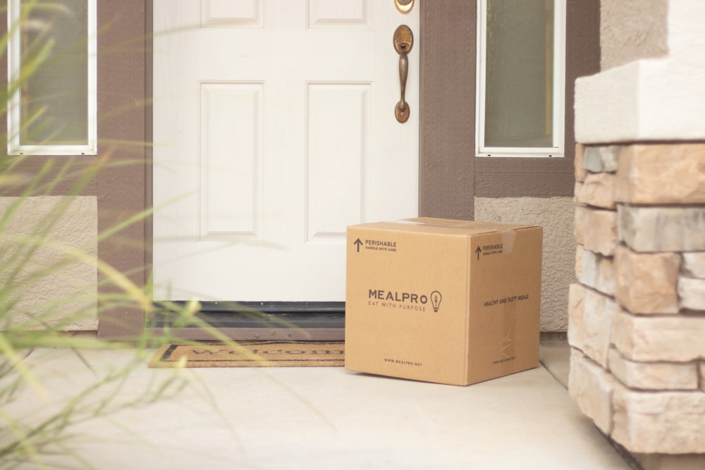 brown cardboard box beside white wooden door