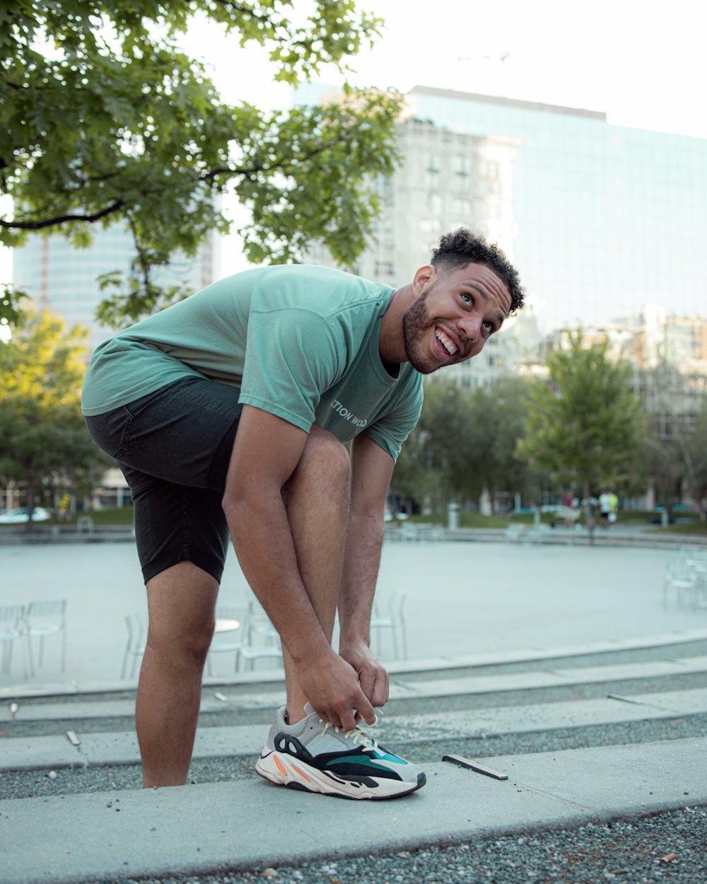 man in green t-shirt and black shorts doing push up on the street during daytime