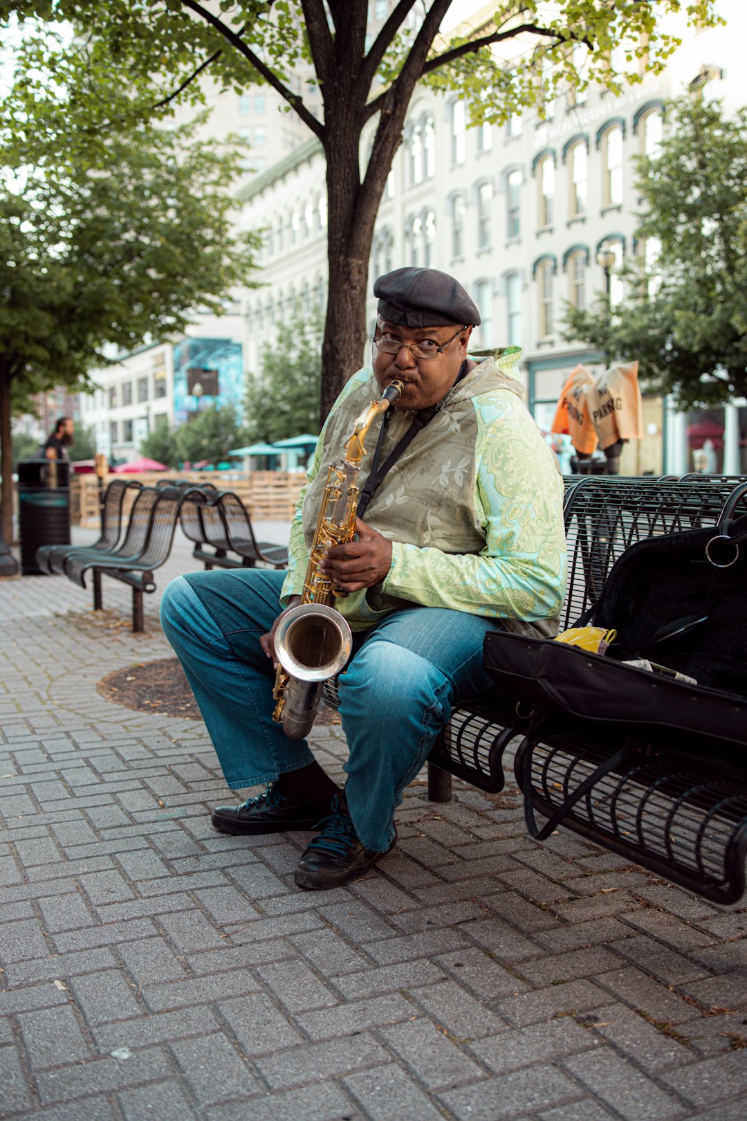 man in green dress shirt playing saxophone sitting on bench during daytime