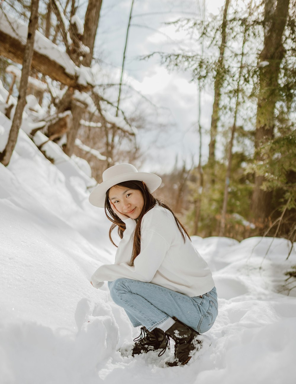 woman in white jacket and black pants sitting on snow covered ground during daytime