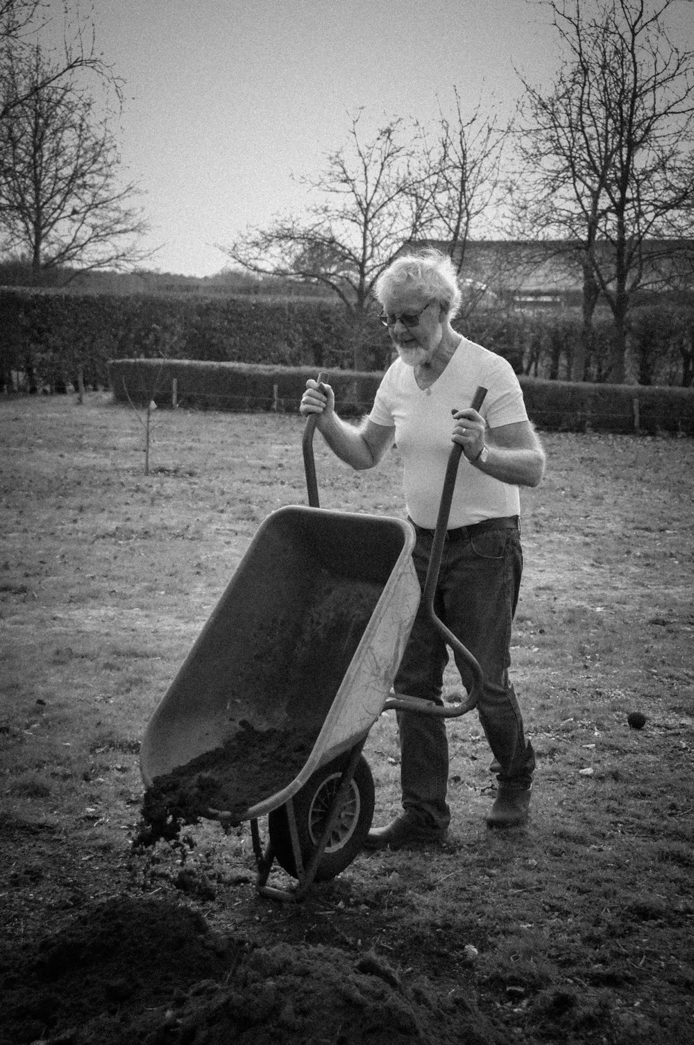 grayscale photo of man in long sleeve shirt and pants holding a wheel barrow