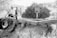 A grayscale image featuring a large piece of agricultural machinery with wheels. The equipment appears to be intended for soil management, as indicated by a logo and text. It is positioned outdoors, surrounded by dry vegetation and a bush in the background.