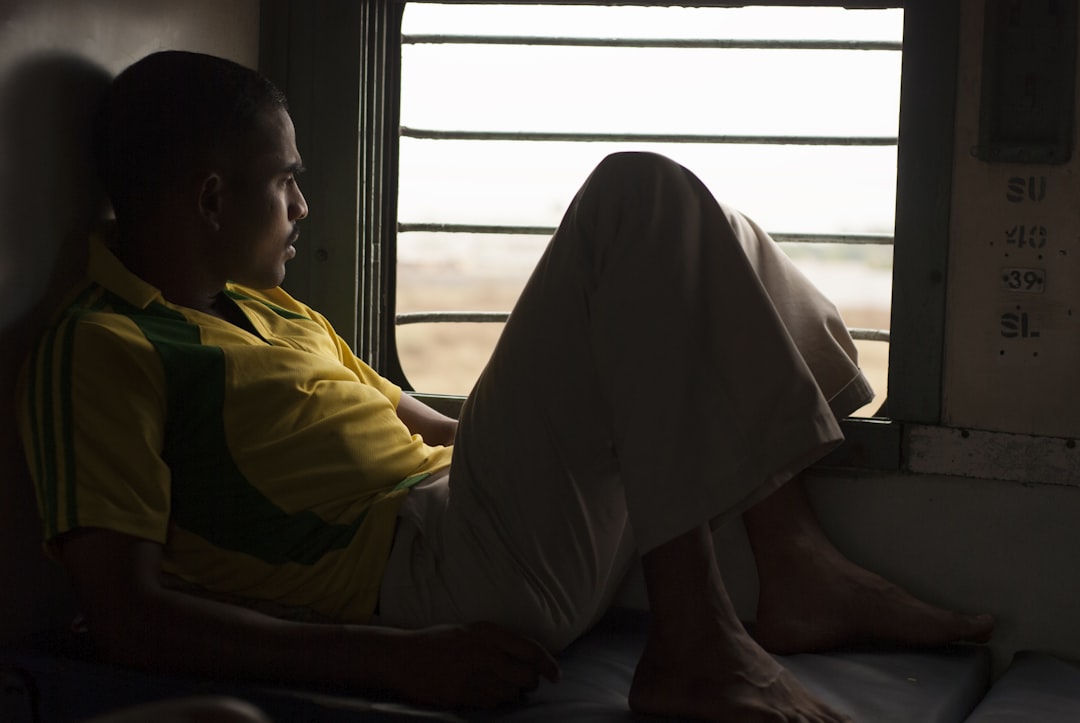 man in yellow shirt sitting on floor, Young Indian man deep in thought looking out the window of a sleeper class train o
