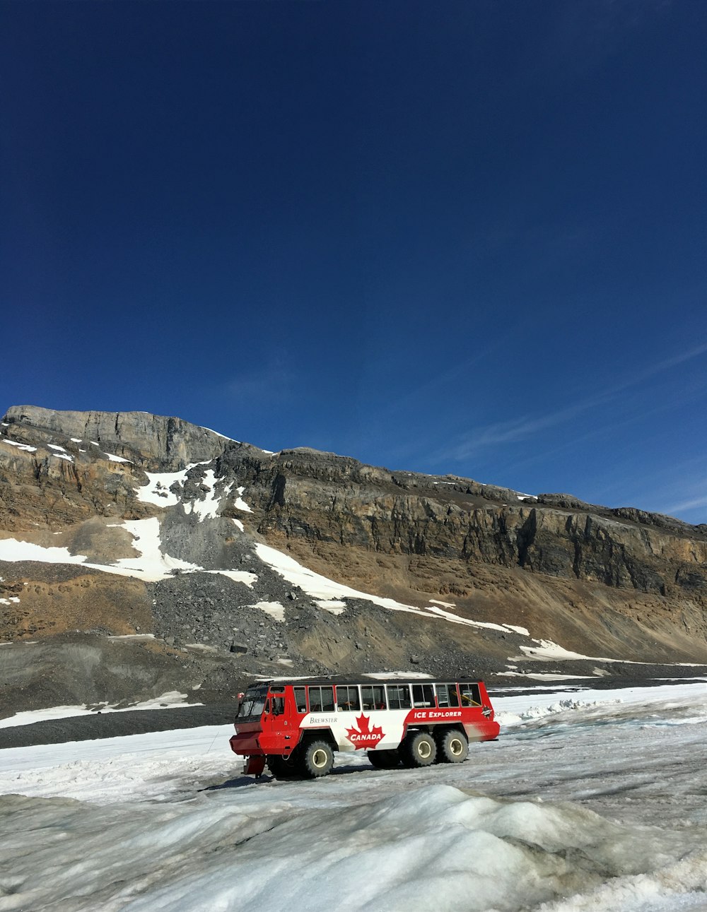 red and white car on snow covered road near rocky mountain during daytime