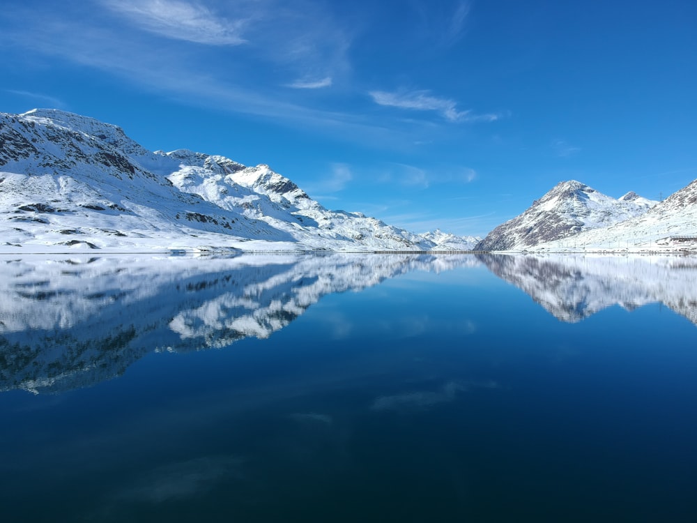 昼間の青空の下、湖畔の雪に覆われた山