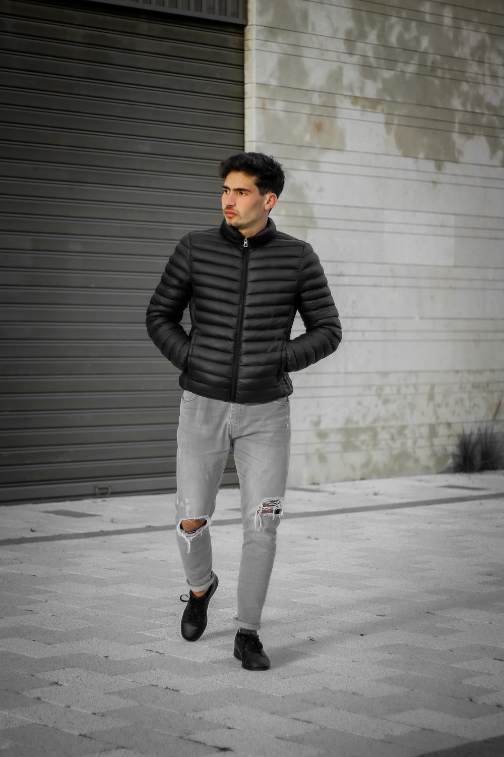 man in black leather jacket and white pants standing on gray concrete floor