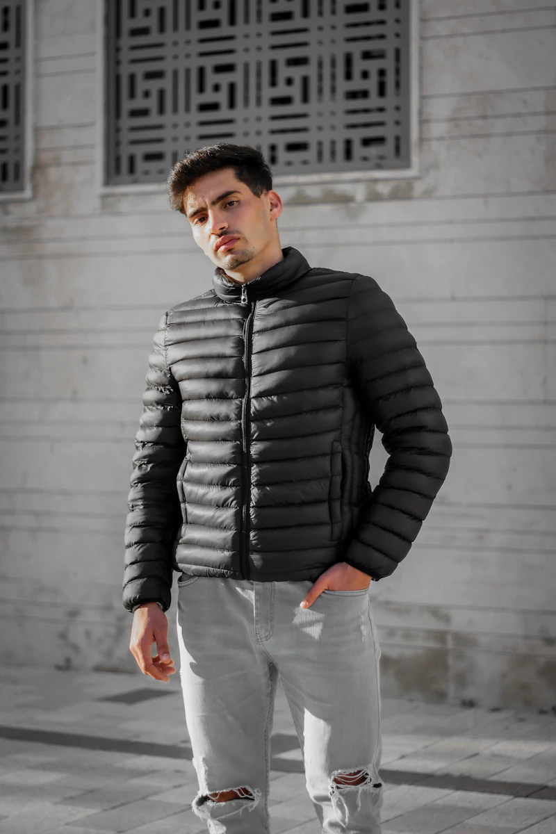 Man in a black quilted puffer jacket against a concrete wall