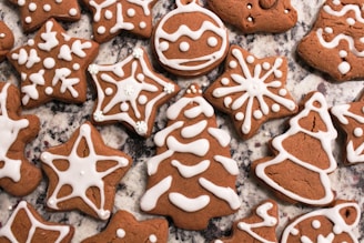 Gingerbread cookies decorated with white icing in various shapes such as stars, trees, and bells. They are placed on a granite countertop, showcasing intricate icing patterns that resemble snowflakes and ornaments.