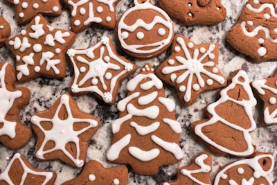 Gingerbread cookies decorated with white icing in various shapes such as stars, trees, and bells. They are placed on a granite countertop, showcasing intricate icing patterns that resemble snowflakes and ornaments.
