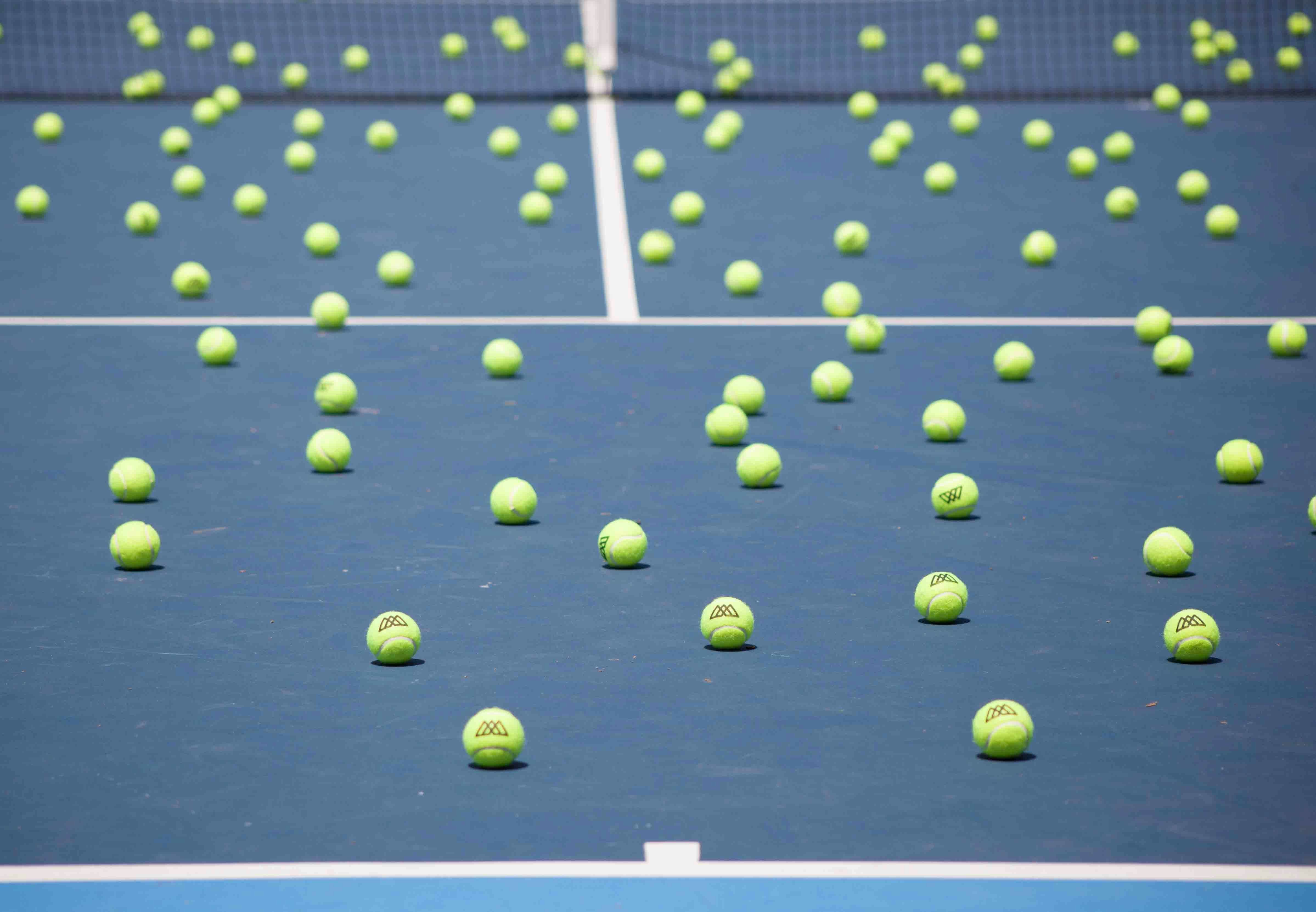 Bunch of tennis balls scattered around blue tennis court