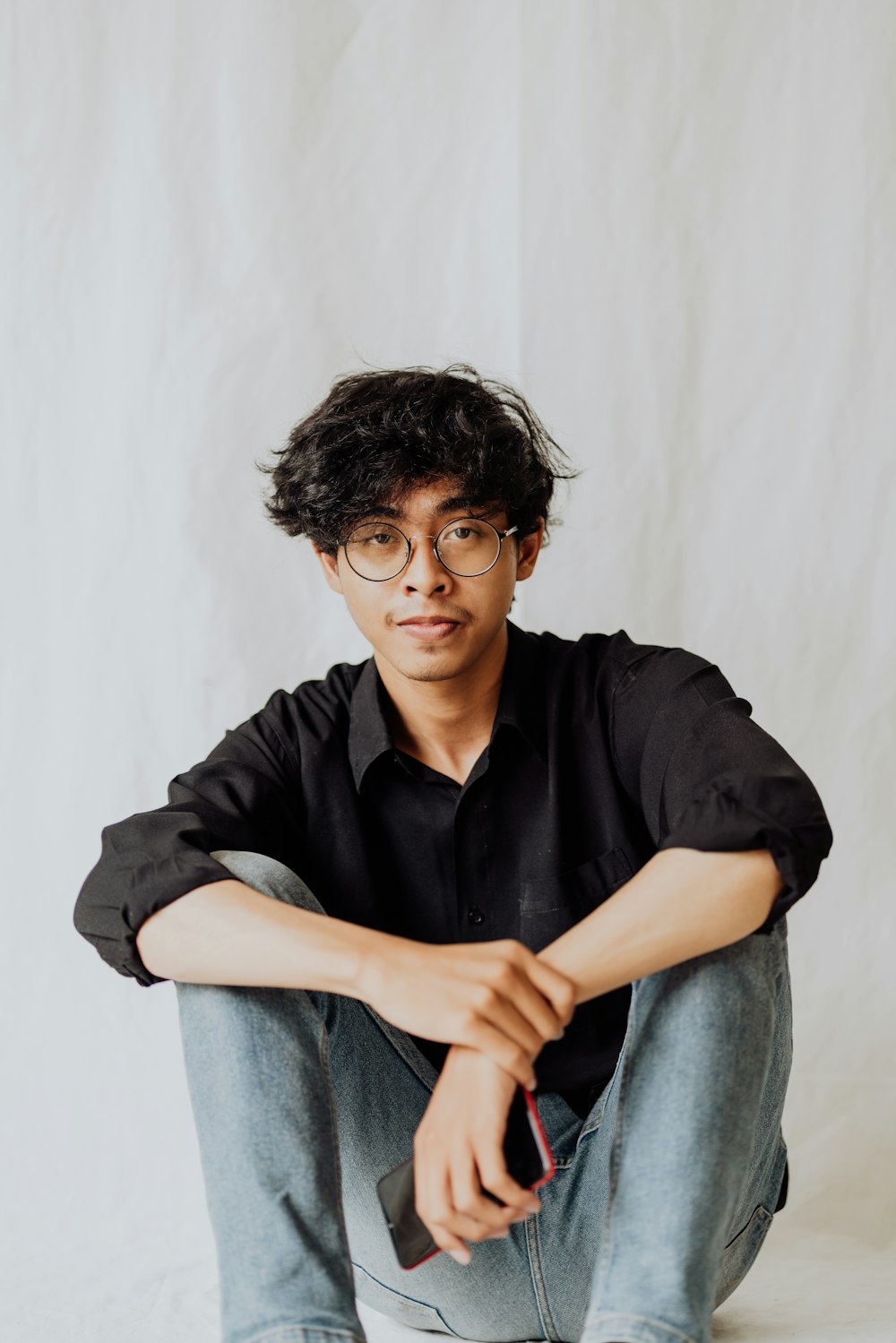 man in black polo shirt and blue denim jeans sitting on white textile