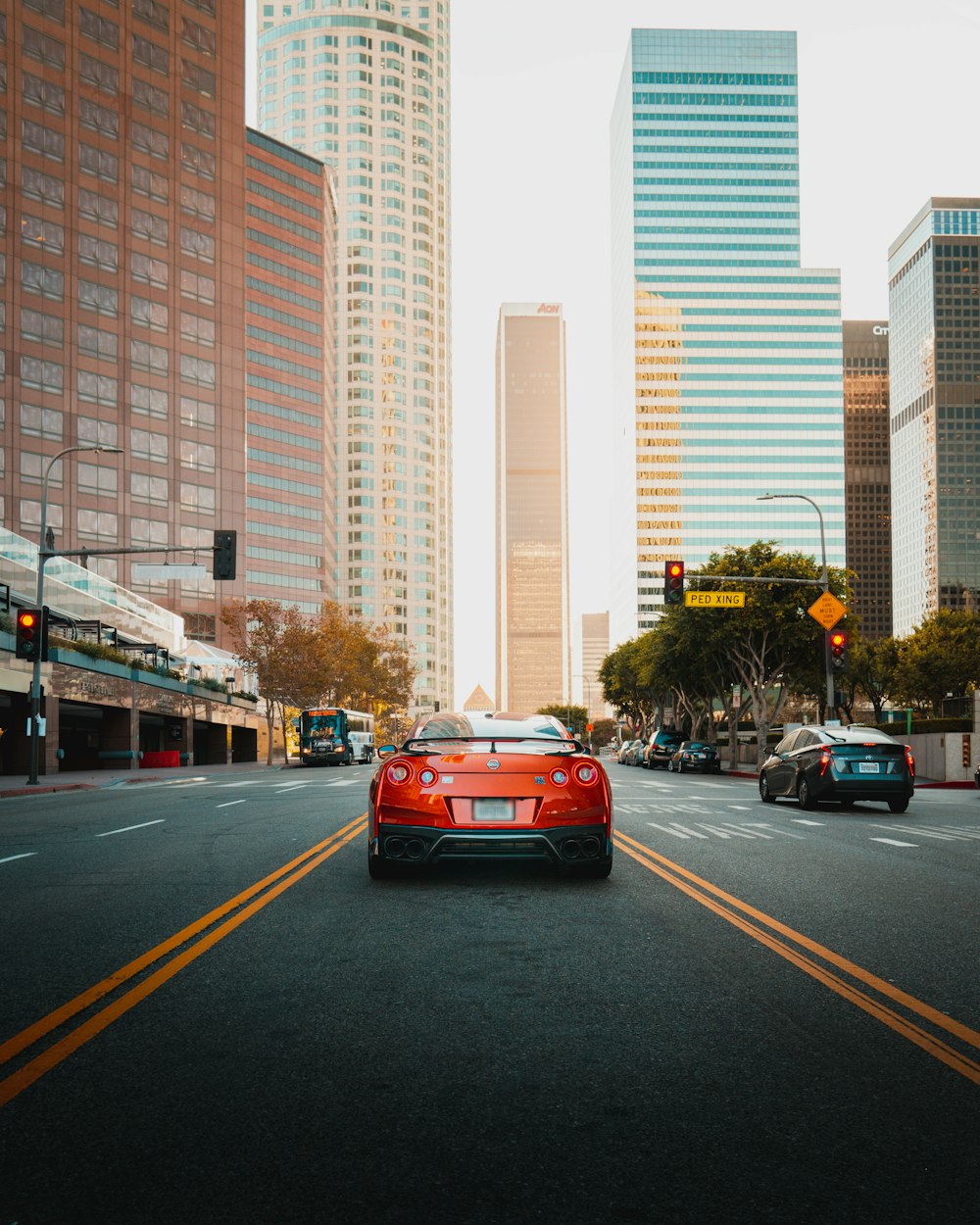 昼間、高層ビルの近くの道路を走る赤い車