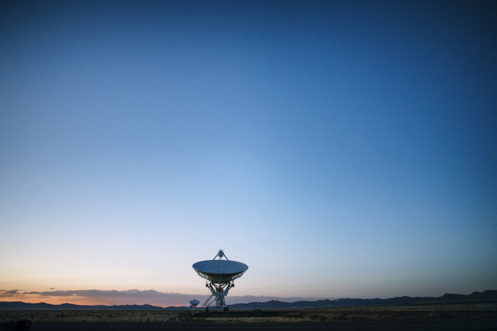 昼間の青空の下、茶色の野原に白い衛星放送受信アンテナ